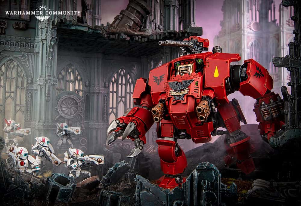A red Brutalis Dreadnought stands amidst ruins, wielding a weapon. White-armored Space Marines approach cautiously from the left. The scene depicts a battle scenario with gothic architecture in the background, capturing the intensity of this latest release.