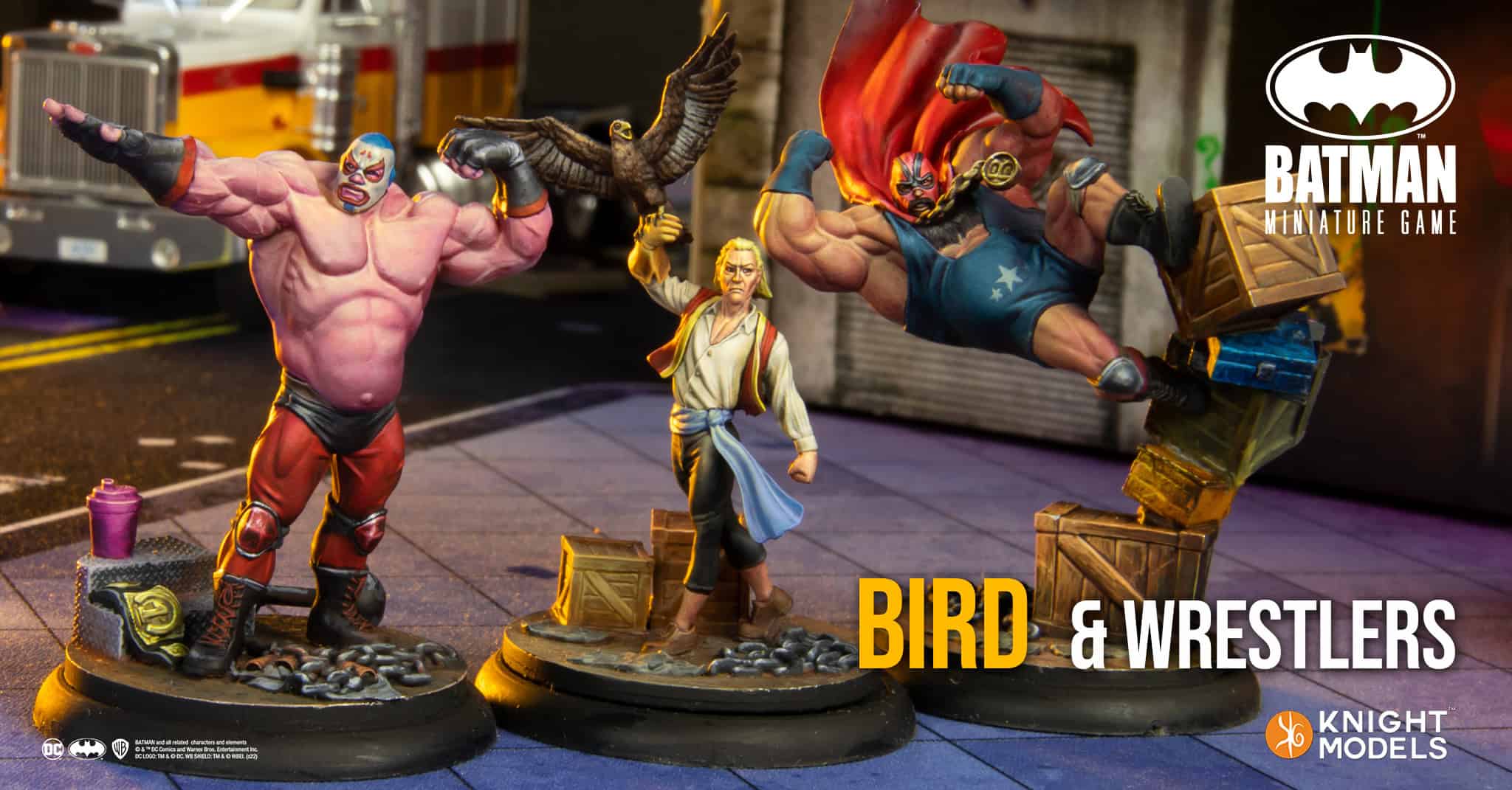 On display are three new miniatures for the Batman Miniature Game by Knight Models. The figures include two wrestlers and a person holding a bird, set against an urban backdrop featuring boxed crates and a vehicle. Text reads "BIRD & WRESTLERS.